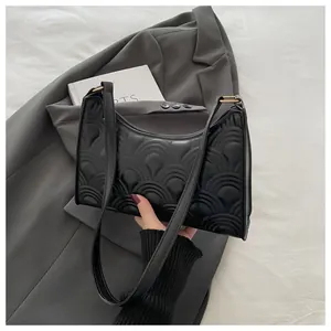 Close-up of black glossy faux leather underarm bag with unique scale-like quilted texture
