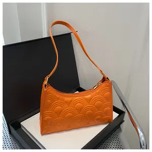 Close-up of orange quilted underarm bag featuring fish scale texture and gold hardware