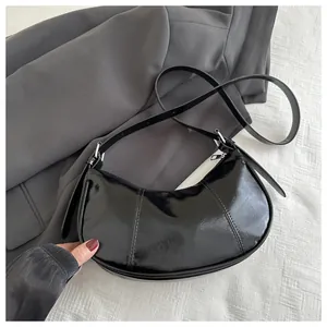 Détail du sac croissant en cuir verni noir avec coutures blanches et finitions argent