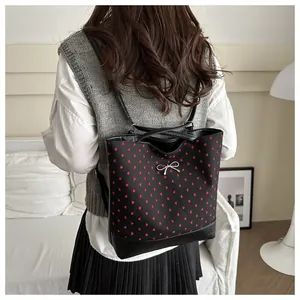 Close-up of black backpack with red hearts and silver bow charm on a model's shoulder