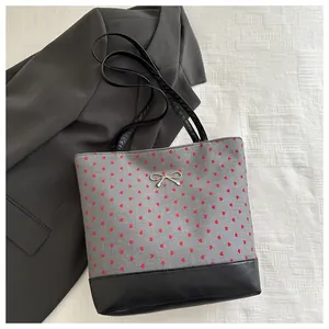 Detailed shot of grey tote with red heart embroidery, black leather base and bow detail
