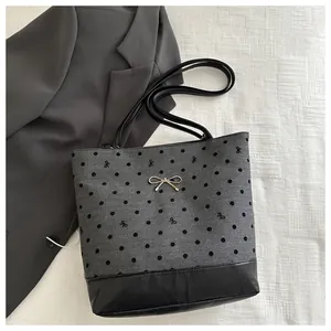Close-up of polka dot tote bag featuring a metallic bow pendant and contrast leather bottom