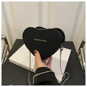 Détail d'un mini sac cœur en cuir noir avec inscription dorée et fine chaîne argentée
