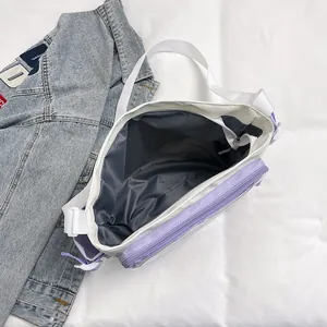 Large beige nylon tote bag with purple pockets and wide strap on denim jacket