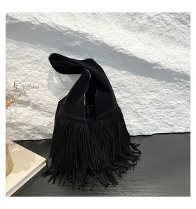 Close-up of black suede tote bag with long fringe details on a textured background