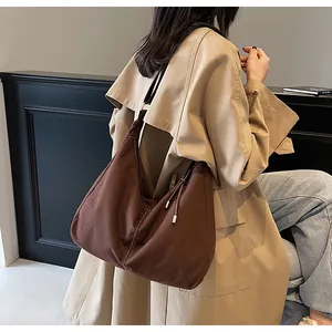 Detail van donkerbruine hobo schoudertas met kwastje gedragen met een beige trenchcoat