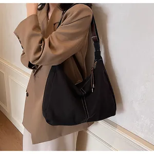Detail van zwarte canvas shopper met witte stiksels en bruine lederen schouderriem