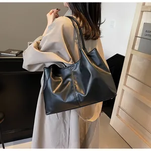 Large black pleated tote bag in soft synthetic leather worn by a model in a trench coat