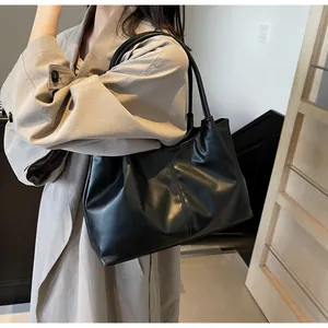 Black pleated tote bag in matte faux leather shown on shoulder with a beige trench coat