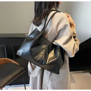 Detail of a black pleated tote bag in soft leather carried by a model in a trench coat