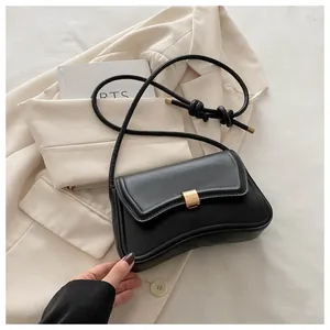 Detail of a black leather square bag with gold buckle on a beige blazer background