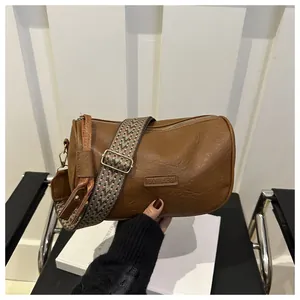 Close-up of brown pillow bag with patterned wide strap and gold hardware detail