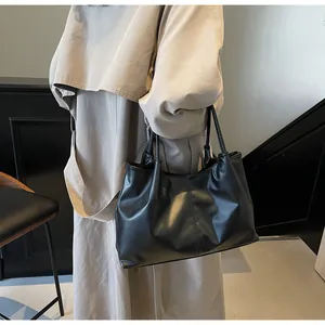 Detail of black pleated tote bag with vertical stitching and slim handles on beige trench coat