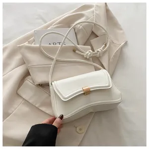 Close-up of a white minimalist shoulder bag featuring a gold buckle and knotted strap detail