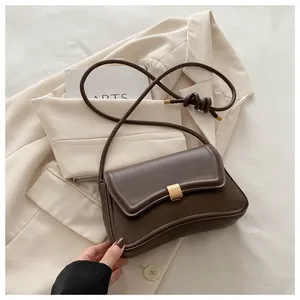 Detailed view of brown leather shoulder bag with gold clasp on a beige suit