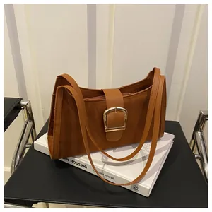 Detail of brown suede shoulder bag with gold horseshoe buckle on art book