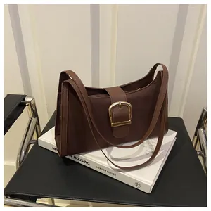 Detail shot of a brown textured faux leather underarm bag with a gold metal buckle closure