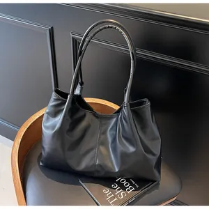 Detail of a black pleated tote bag with glossy finish on a leather chair