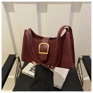 Detail of burgundy suede underarm bag with decorative gold buckle and dual leather straps