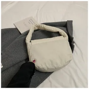 Close-up of a cream quilted puffer cloud bag with soft padded handle on a bed