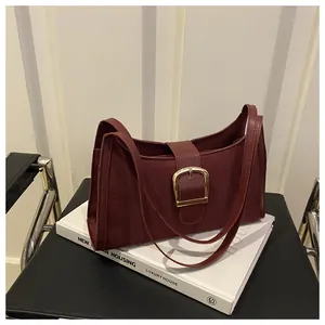 Close-up of a burgundy suede underarm bag with a vintage gold metal buckle on a white book