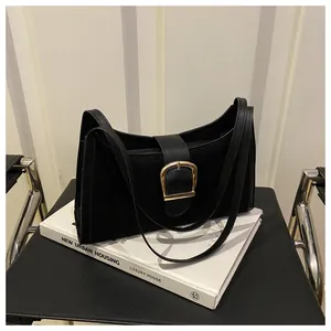 Detail of black suede shoulder bag with gold metal buckle on white books background