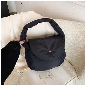 Detail of black quilted puffer shoulder bag with silver button on a minimal background
