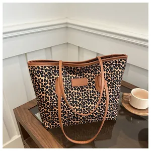 Detailed close-up of leopard print canvas tote bag with brown leather handles on wooden table