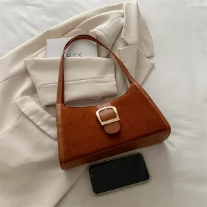 Brown suede underarm bag with a large gold metal buckle on a beige blazer background