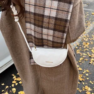 White croissant shoulder bag with woven strap shown in autumn scenery with ginkgo leaves