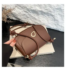 Detail of dark brown saddle bag featuring oval gold buckle and knotted braided shoulder strap