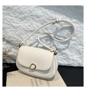 Detail of white saddle bag featuring a gold ring buckle and knotted cord strap
