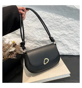 Detail of black saddle bag featuring gold irregular metal buckle and knotted strap design
