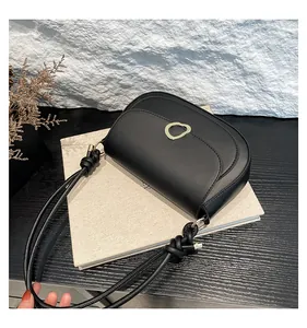 Detail of a black matte saddle bag featuring a golden metal buckle and knotted strap