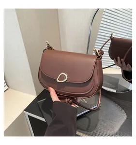 Detail view of dark brown saddle bag with unique gold metal clasp and matte leather texture