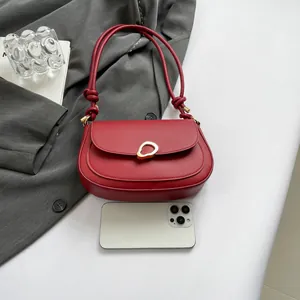 Minimalist red saddle bag with gold metal buckle and leather strap shown with smartphone