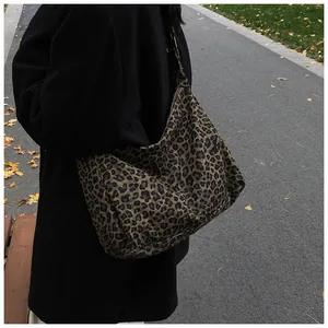Detailed side view of large leopard print canvas hobo bag worn by a model in park
