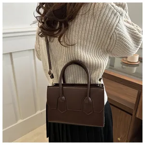 Detail of a deep brown rectangular leather bag with elegant stitching and metallic strap buckles