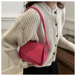 Detail view of pink shoulder bag with textured flap and knotted strap on knit cardigan