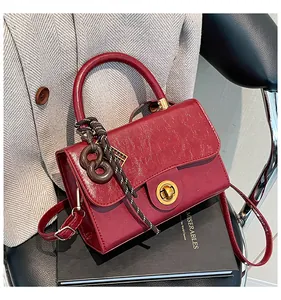 Détail d'un sac à main en cuir verni bordeaux avec fermoir doré et breloque tissée