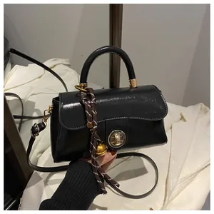 Dettaglio borsa nera lucida con chiusura a scatto dorata e ciondolo a campanello