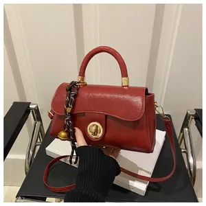 Dettaglio borsa in pelle lucida rossa con chiusura a anello dorata su libro bianco