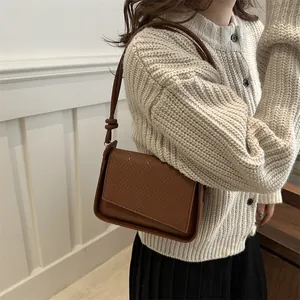 Brown woven texture underarm bag with knotted shoulder strap worn with knit cardigan