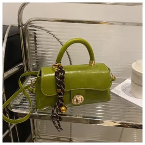 Dettaglio della borsa a tracolla verde avocado con hardware dorato e ciondolo su scaffale