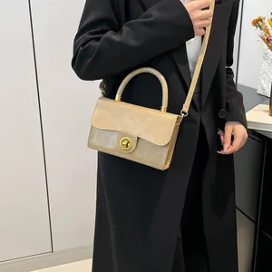 Sac à main en cuir verni kaki avec fermoir doré porté par un mannequin en tailleur