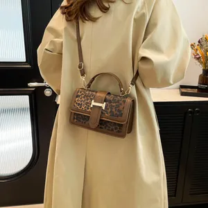 Leopard print crossbody handbag with gold H-clasp held by a model in a beige trench coat