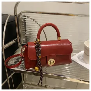 Dettaglio borsa rosso scuro vintage con chiusura dorata rotonda e ciondolo campanello