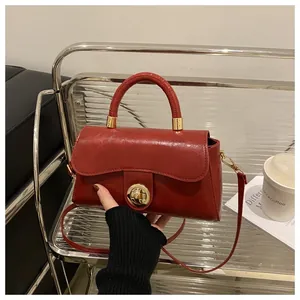 Dettaglio della borsa in pelle rosso scuro con chiusura dorata su supporto argento moderno