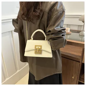 Detail of cream crossbody bag featuring a gold buckle and chain on a brown jacket
