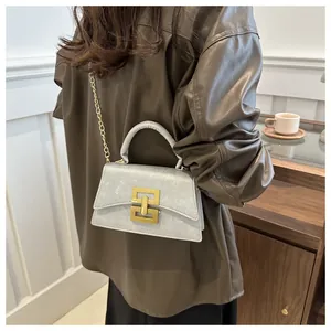 Detail of light blue textured crossbody bag with gold geometric clasp and chain strap
